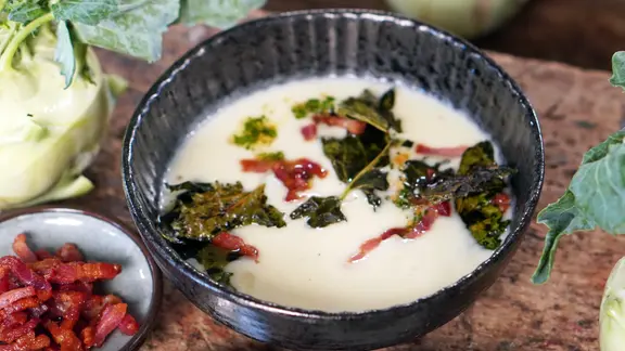 Ein Schälchen mit einer Kohlrabi-Suppe getoppt mit Kohlrabiblättern und Speckstreifen.
