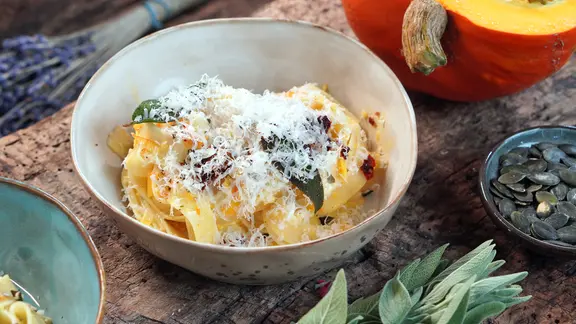 Eine Schüssel mit Kürbispasta und Käse, daneben: Kürbis, Salbei und Kürbiskerne