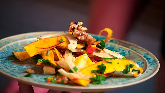 EIn Kürbissalat, garniert mit Kräutern und Nüssen.