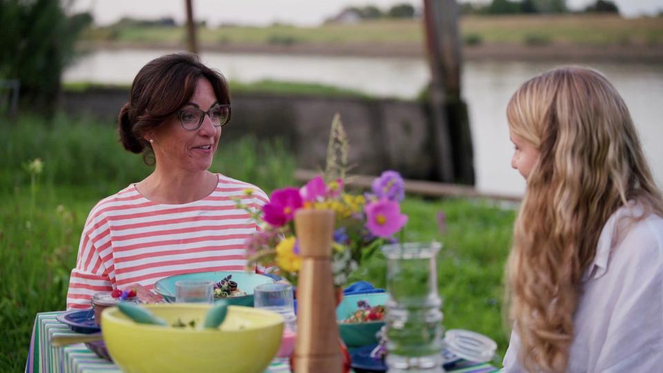 Dr. Schäfer und ihre Patientin sitzen beim Camping am reich gedeckten Esstisch.